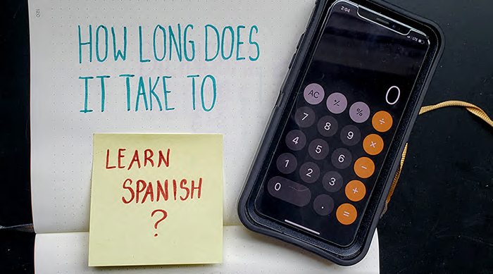 Several notebooks which make up the word "how long does it take to learn Spanish?" with a calculator next to it