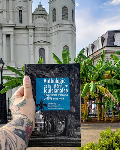 A hand holding a French book in front of palm trees and an old-looking church